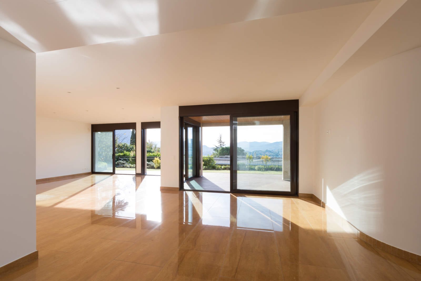 Ein geräumiger, leerer Raum mit polierten Holzböden und großen, raumhohen Fenstern bietet einen atemberaubenden Blick auf Grün und Berge. Die kürzlich erfolgte Sanierung sorgt für reichlich Tageslicht und schafft eine helle Atmosphäre, die sich perfekt für jedes Innenausbauprojekt eignet.